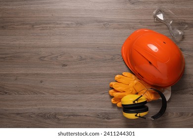 Hard hat, gloves, goggles and earmuffs on wooden table, flat lay with space for text. Safety equipment - Powered by Shutterstock