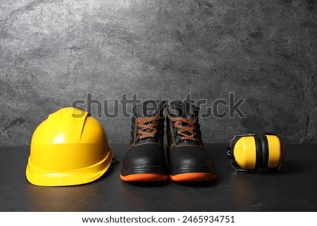 Hard hat, pair of working boots, and earmuffs on gray background, space for text