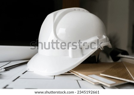 Hard hat safety helmet, used in industrial workplace. Worker head protection from injury on a construction site. Design studio composition, with structural blueprint projects plans and wood samples.