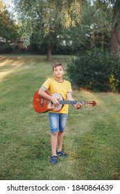 Hard Of Hearing Preteen Boy Playing Guitar Outdoor. Child With Hearing Aids In Ears Playing Music And Singing Song In Park. Hobby Art Activity For Children Kids. Authentic Childhood Moment. 