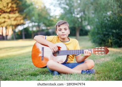 Hard Of Hearing Preteen Boy Playing Guitar Outdoor. Child With Hearing Aids In Ears Playing Music And Singing Song In Park. Hobby Art Activity For Children Kids. Authentic Childhood Moment. 