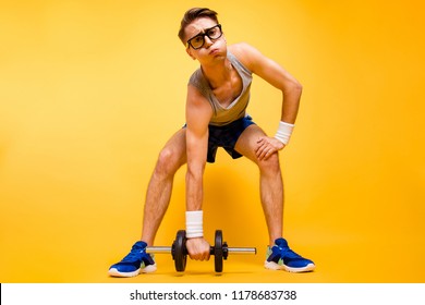 It's too hard for me! Full length, legs, body, size portrait of youth man look at camera can not lift dumbbells from the floor isolated on vivid yellow background
