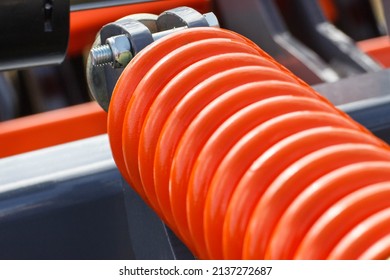 Hard orange spring made of steel. Part of big industrial or agricultural machine. Technology