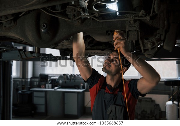 Hard to see some things. Man at\
the workshop in uniform fixes broken parts of the modern\
car.