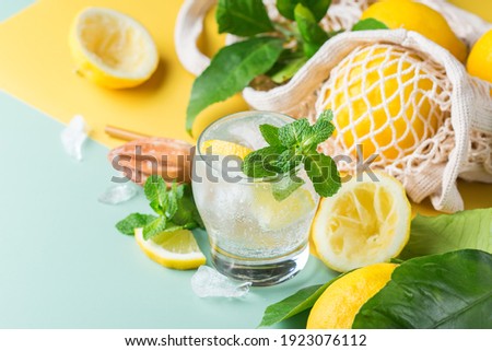 Hard seltzer cocktail with lemon, mint and ice on a table. Summer refreshing beverage, drink with trendy zero waste accessories, bamboo straw and mesh bag.