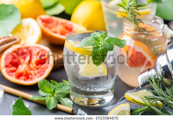 Hard seltzer\
cocktails with lemon, grapefruit, mint, rosemary and ice on a\
table. Summer refreshing beverage, drink with trendy zero waste\
accessories, bamboo straw and mesh\
bag.