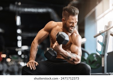 Hard strength workout. Naked bodybuilder exercising with dumbbell at gym, empty space