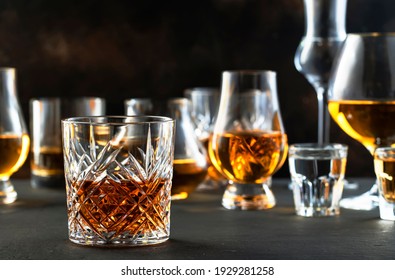 Hard strong alcoholic drinks and distillates in glasses in assortment: vodka, cognac, tequila, scotch, brandy and whiskey, grappa, liqueur, vermouth, tincture, rum. Brown background