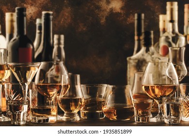 Hard strong alcoholic drinks and distillates in glasses and bottles in assortment: vodka, cognac, tequila, scotch, brandy and whiskey, grappa, liqueur, vermouth, tincture, rum. Brown background