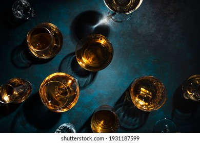 Hard strong alcoholic drinks, spirits and distillates in glasses: vodka, cognac, tequila, scotch, brandy and whiskey, grappa, vermouth, rum. Blue background, top view