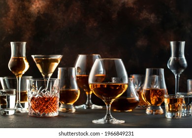 Hard strong alcoholic drinks, spirits and distillates in glasses in assortment: vodka, cognac, scotch, whiskey etc. Brown bar counter background