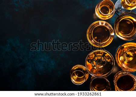 Hard strong alcoholic drinks, spirits and distillates in glasses: vodka, cognac, tequila, scotch, brandy and whiskey, grappa, vermouth, rum. Blue background, top view