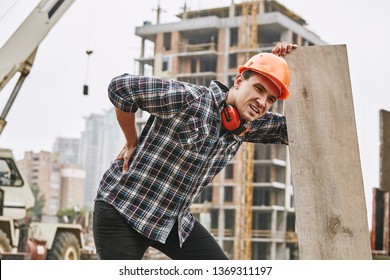 Hard Work. Construction Worker In Protective Helmet Feeling Back Pain While Working At Construction Site. Building Construction. Pain Concept