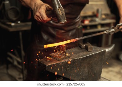 Hard work. Energy and power. Close-up working powerful hands of male blacksmith forge an iron product in a blacksmith. Hammer, red hot metal and anvil. Concept of labor, retro professions - Powered by Shutterstock