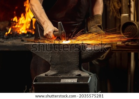 Hard work. Energy and power. Close-up working powerful hands of male blacksmith forge an iron product in a blacksmith. Hammer, red hot metal and anvil. Concept of labor, retro professions