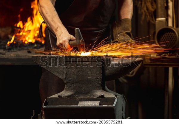 Hard\
work. Energy and power. Close-up working powerful hands of male\
blacksmith forge an iron product in a blacksmith. Hammer, red hot\
metal and anvil. Concept of labor, retro\
professions