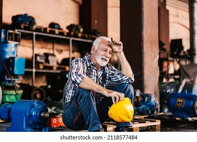 Hard work in metallurgy and heavy industry. A tired senior heavy industry worker is sitting on the pallet next to a machine at the facility, taking a break and wiping sweat from his forehead. - Powered by Shutterstock