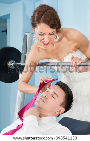 Hard work for newlyweds - bride wiping off sweat from groom's forehead. Gym used to illustrate the concept