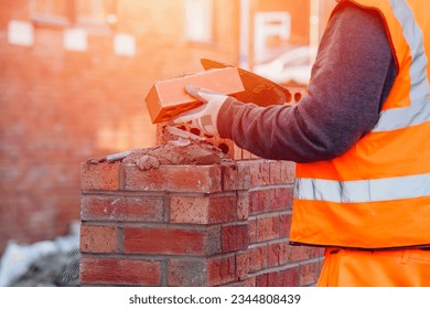 Hard working bricklayer lays bricks on cement mix on construction site. Fight housing crisis by building more affordable houses concept
