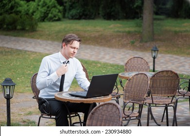 Hard Working Businessman. Attractive Young Tired Man In Formal Shirt And Tie Working On Laptop While Sitting At The Table Outdoors