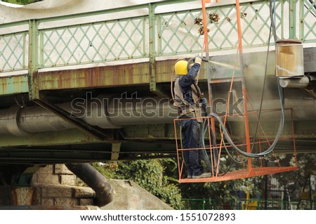 Hard working man is sandblasting the iron bridge. Sandblasting the bridge. Removing rust off the bridge. Preparing the bridge for painting.