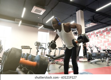 Hard Workout. Muscular Black Man Wearing Sportswear Doing Exercises With Dumbbells For Back At Gym