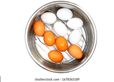 Hard-boiled chicken eggs, white and brown, are laid out on a trivet in a metal pot. Cooking eggs in an electrical pressure cooker concept. 