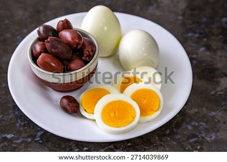 Hard-boiled eggs, sliced egg, and black olives on a white plate with an egg slicer