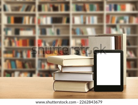 Hardcover books and modern e-book on wooden table in library. Space for text