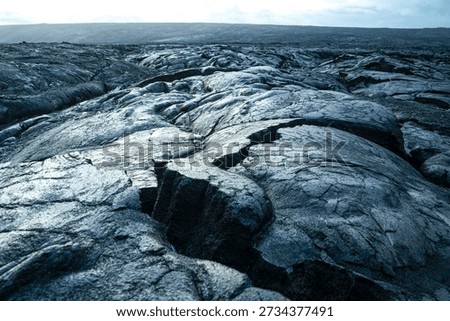 Hardened lava flow forming dramatic rock textures across a volcanic landscape on the Big Island, Hawaii, United States, under overcast sky.