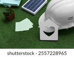 Hardhat with house model, sticky notes and plant on grass, closeup. Green Energy concept