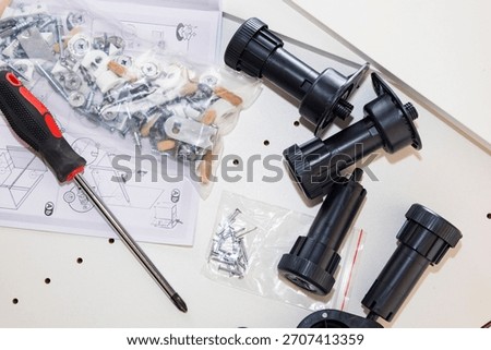 Hardware assembly kit with black standoffs scattered across light tabletop, assorted screws and plastic anchors, instruction sheet, red-handled screwdriver,
