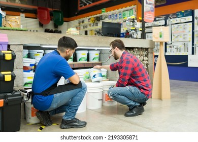 Hardware Store Worker And Young Man Seen From Behind Looking To Buy A Bucket Of Paint Or Waterproofer At The Shop