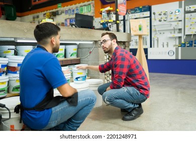 Hardware Store Worker And Young Man Seen From Behind Looking To Buy A Bucket Of Paint Or Waterproofer At The Shop