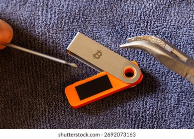 Hardware wallet being physically attacked indoors using screwdriver and pliers. Physical device vulnerability concept.