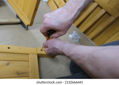 Hard-working Adult Man, Senior 60-65 Years Old Assemble Wooden Furniture From Parts At Home, Tightens Screws With Screwdriver, Assembling Garden Bench, New Furniture Assembly Concept, Moving, Hobby