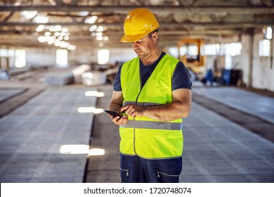 Hardworking Blue Collar Worker Standing At Construction Site And Using Smart Phone To Order Some More Materials For Building.