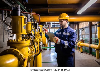 Hardworking Caucasian Engineer Wearing Protective Uniform And Hardhat Checking Gas Pipe Installation Inside Factory.