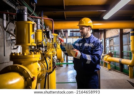 Hardworking caucasian engineer wearing protective uniform and hardhat checking gas pipe installation inside factory.