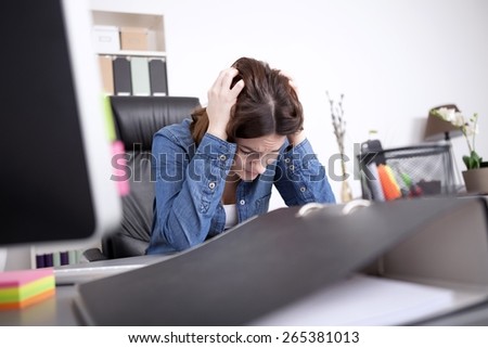 Hardworking dedicated businesswoman sitting at her desk in the office with her head in her hands concentrating on a paper document on the desk in front of her