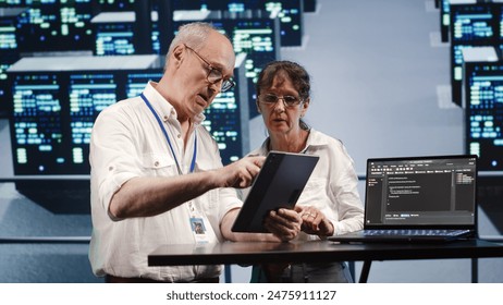 Hardworking engineers in high tech facility, solving tasks on tablet while running scripts on laptop terminal. Dilligent technicians amidst blade servers, accessing databases and manipulating code