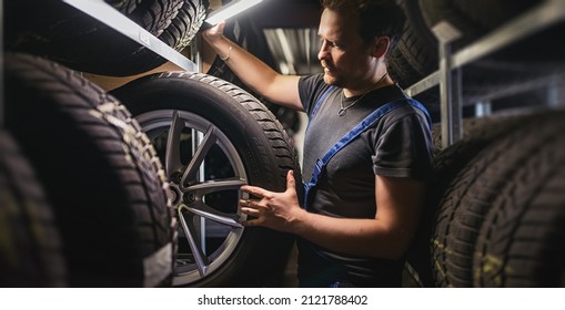 Hardworking experienced worker holding tire and he wants to change it In the tire store. Selective focus on tire.