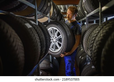 Trabajador experimentado y trabajador con neumáticos y quiere cambiarlo en la tienda de neumáticos. Centrarse selectivamente en el neumático.