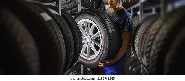 Trabajador experimentado y trabajador con neumáticos y quiere cambiarlo en la tienda de neumáticos. Centrarse selectivamente en el neumático.