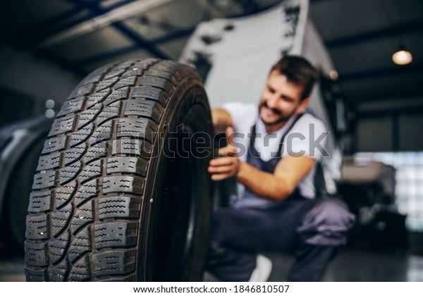 Hardworking\
experienced worker holding tire and he wants to change it. In\
background is truck. Selective focus on\
tire.