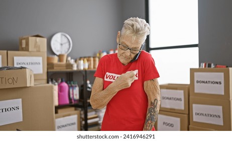 Hard-working, grey-haired senior woman volunteer engrossed in serious phone conversation at community charity center, surrounded by boxes of donations - Powered by Shutterstock