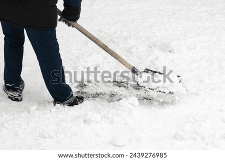A hardworking man clearing away the freshly fallen snow with his trusty iron shovel, complete with a sturdy wooden handle. A close-up view of the snow removal process