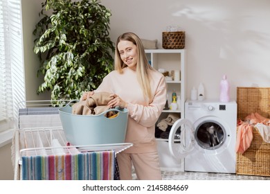Hardworking Organized Girl Cleaning In An Apartment. Woman Stands In Laundry Room By Clothes Dryer, Unpacks Items From Washing Machine And Hangs Them Out To Dry.