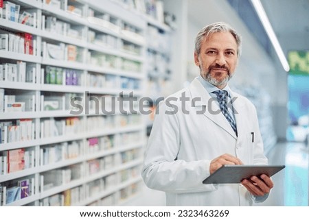 A hardworking senior male pharmacist using a digital tablet while working, looking at the camera.