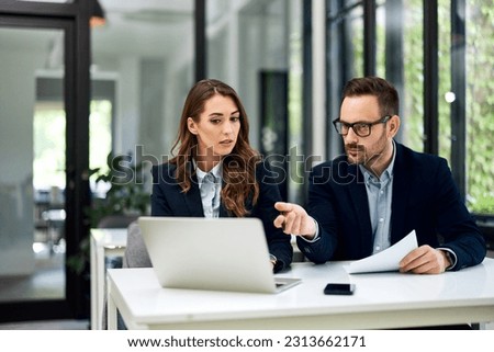 A hardworking and serious female and male employee working together on a new project over a laptop.